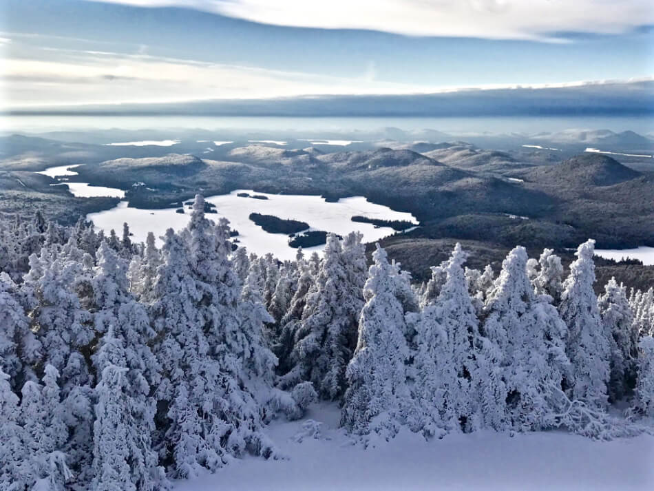 mountain top view showing snow covered trees and several lakes