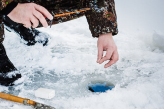 hands of an ice fisherman pulling line out of hole in ice